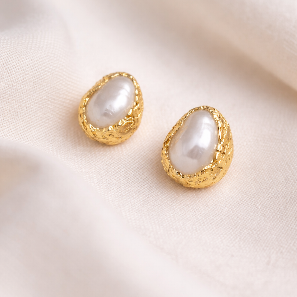 Gold earrings with pearl-like stones on a soft beige background