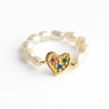 Gold heart-shaped ring with colored stones on a white background