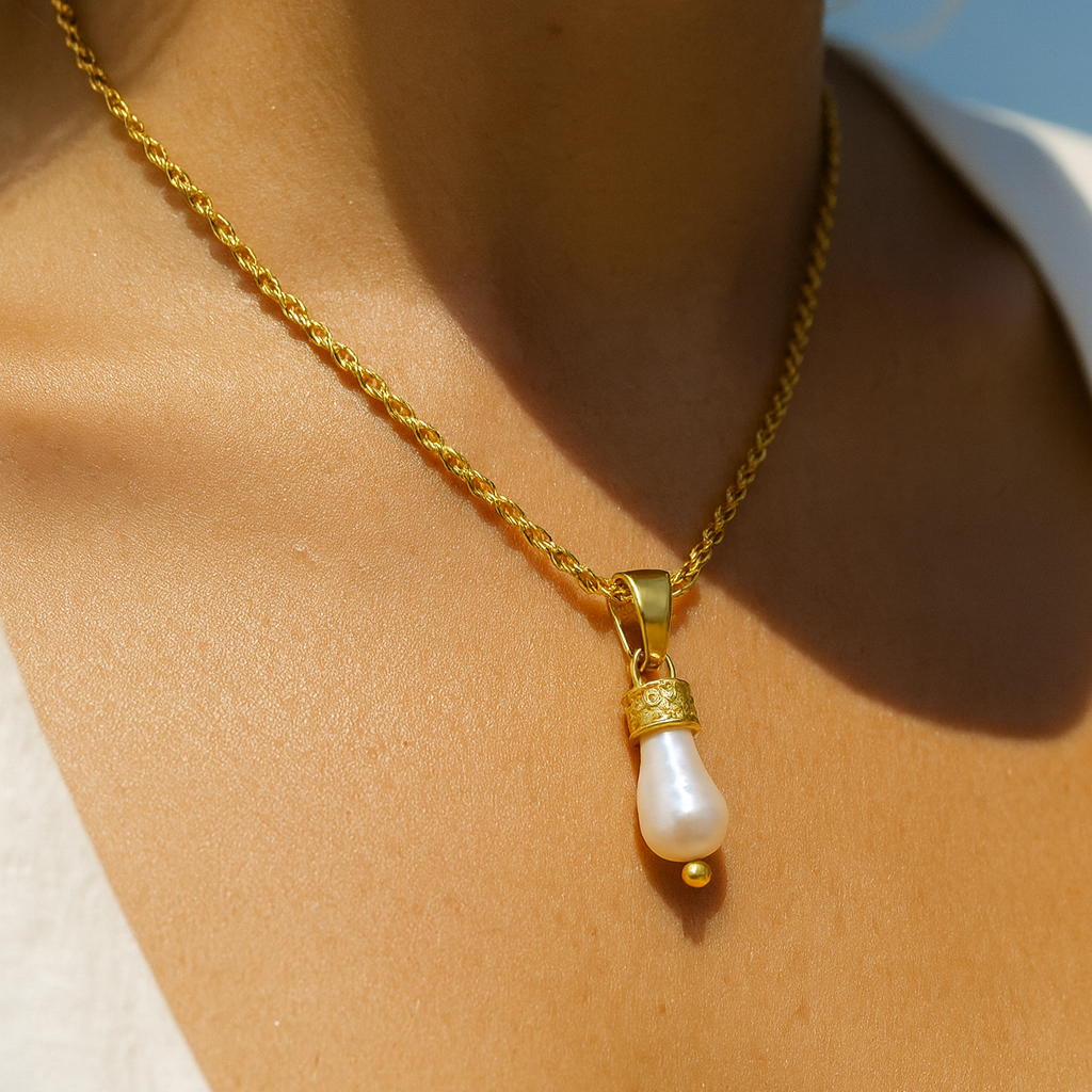 Gold necklace with a pearl pendant on a person against a blue sky.