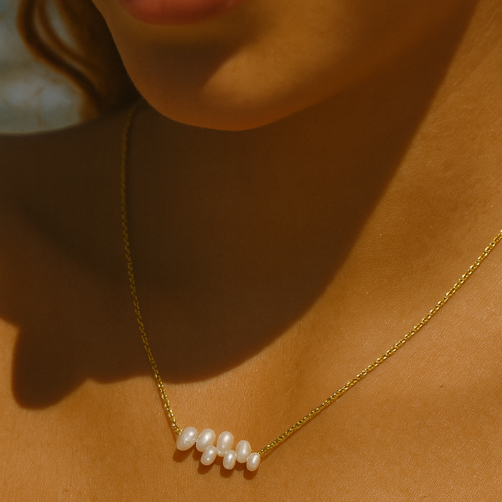 Close-up of a person wearing a gold necklace with pearls on a warm-toned background
