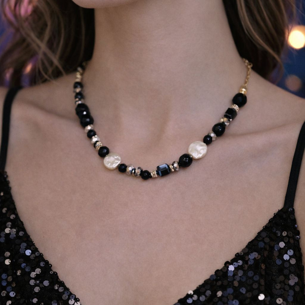 Necklace with black, white, and gold beads worn by a person in a sparkly black top.