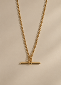 A gold chain necklace with a minimalist horizontal bar toggle pendant, displayed against a neutral beige background.