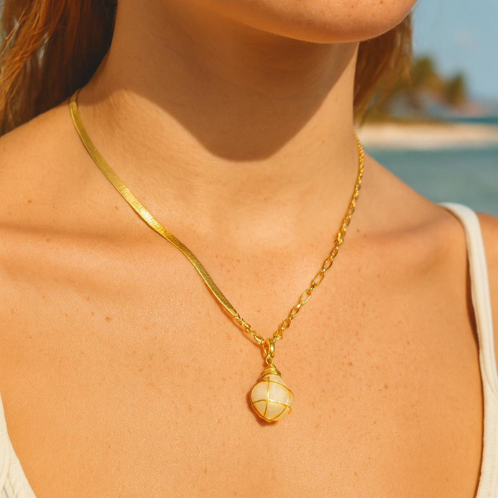 Gold necklace with a pendant worn by a person against a beach background