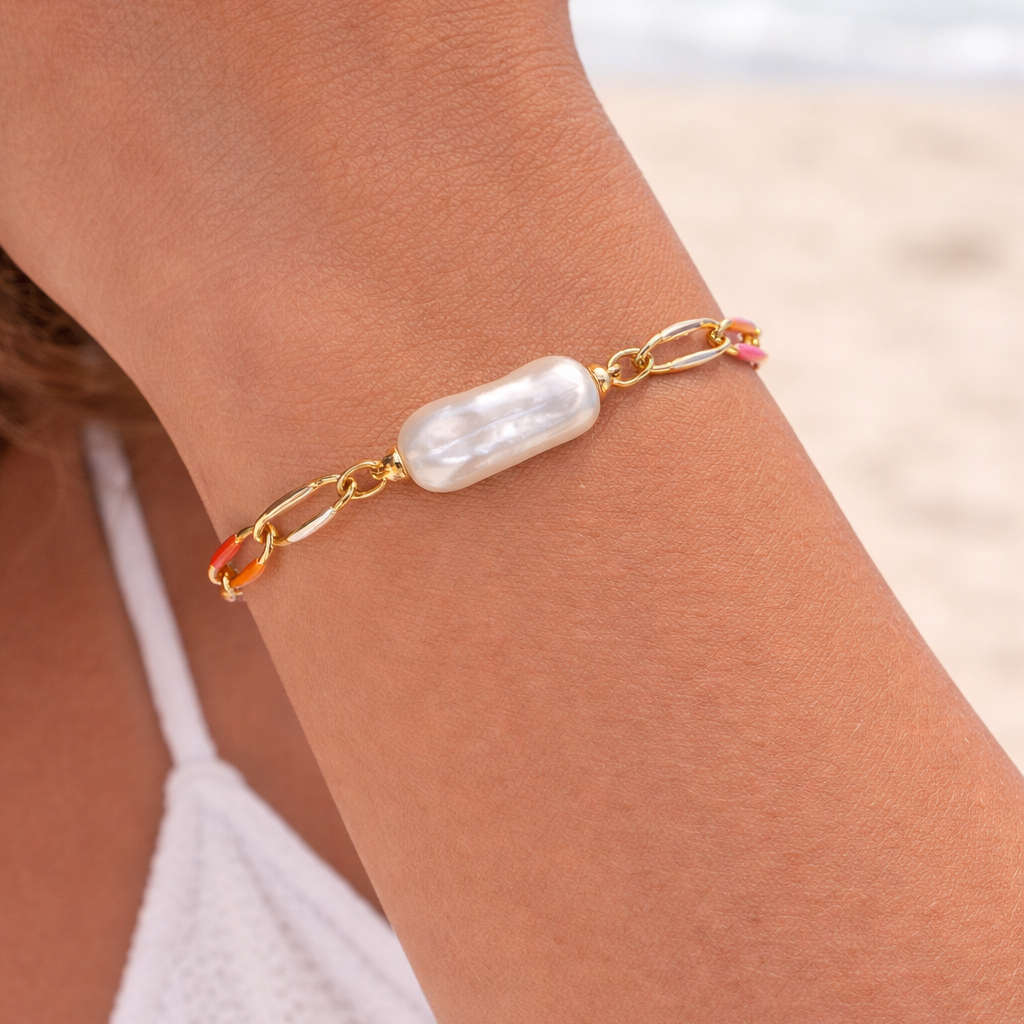 Gold bracelet with a pearl-like bead on a person's wrist against a beach background