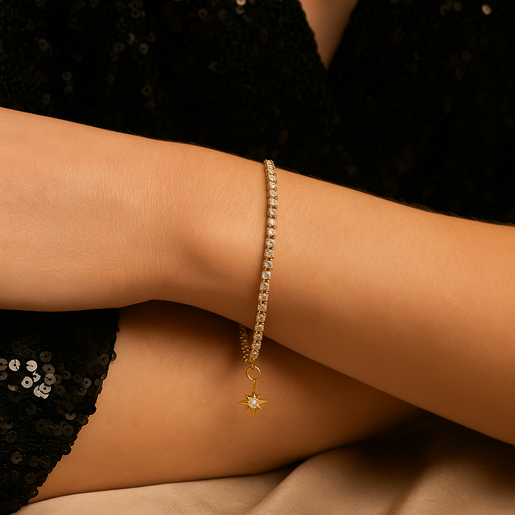 Gold bracelet with a star charm on a person's wrist against a black sequin dress.