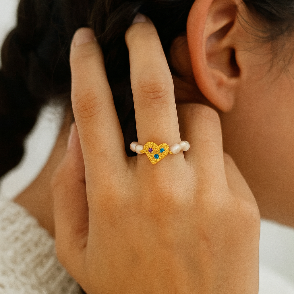 Close-up of a hand wearing a decorative ring with pearls and gemstones, touching hair.