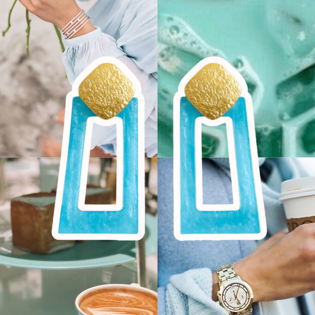 Pair of earrings with gold and blue design held by a hand next to a cup of coffee.