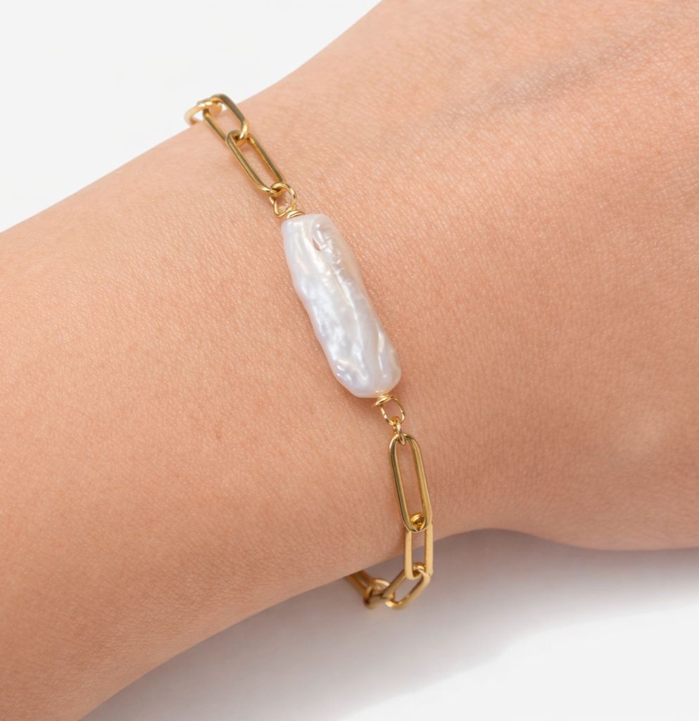 Gold bracelet with a large white pearl on a wrist against a light background