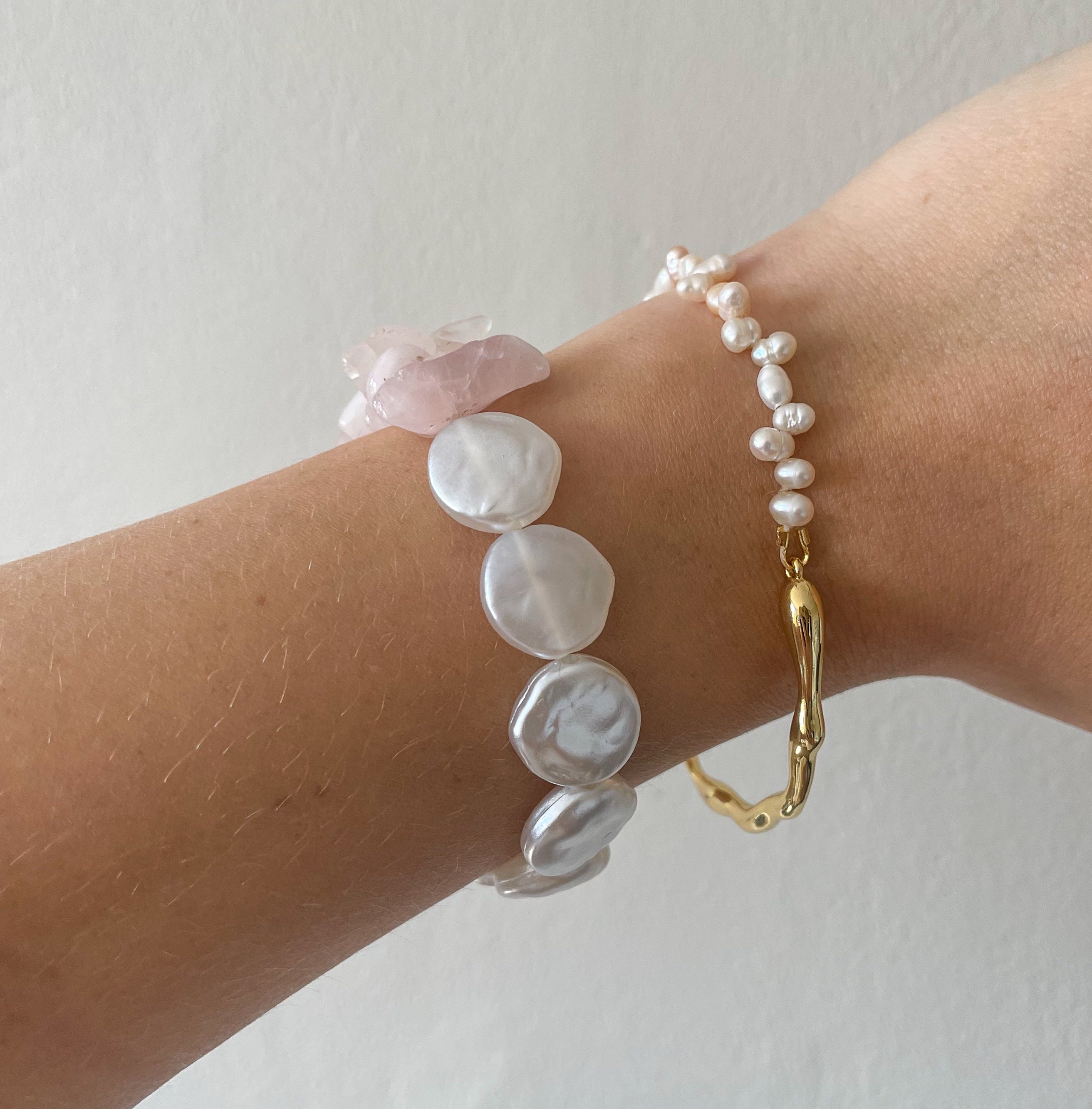 Wrist wearing a gold bracelet and two pearl bracelets on a plain background
