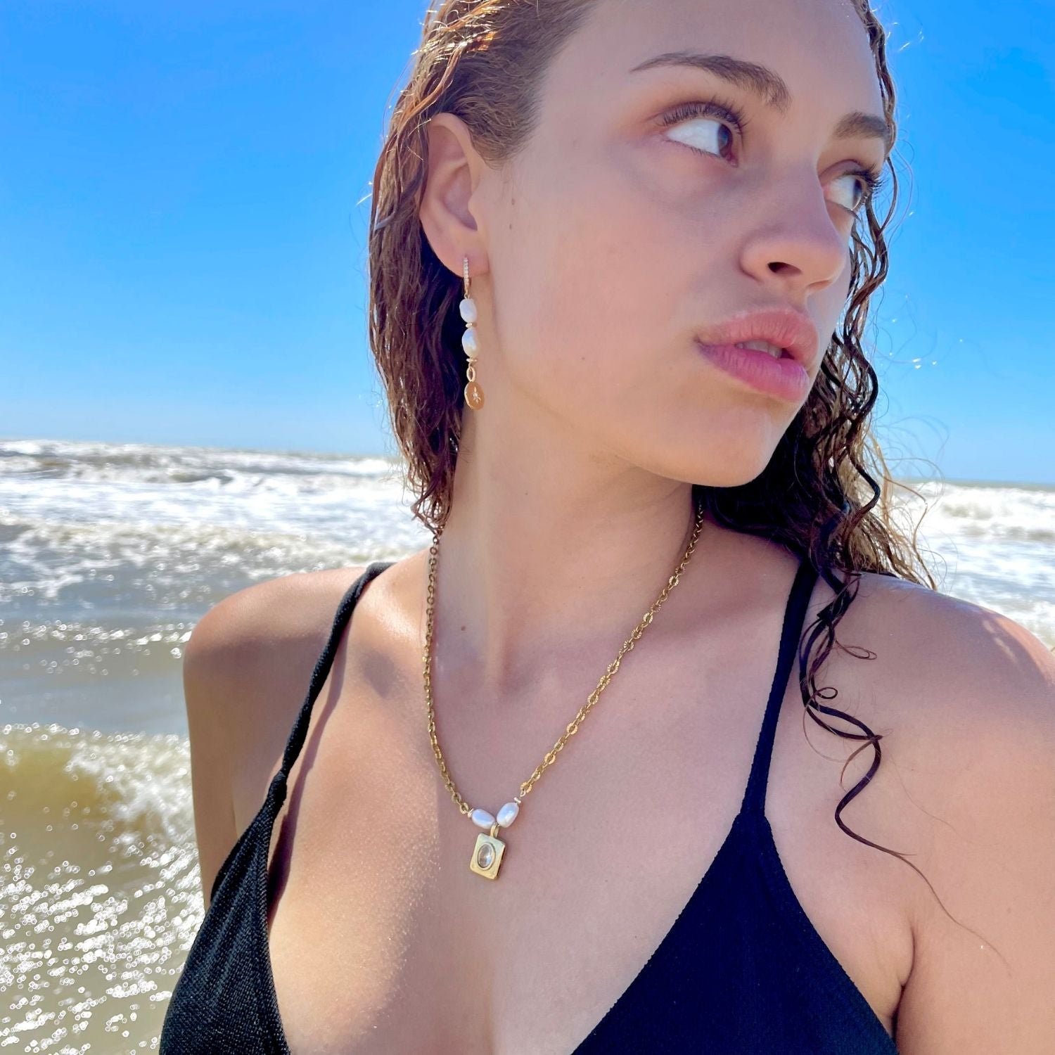 Woman on a beach wearing a black top and gold necklace with a clear sky background