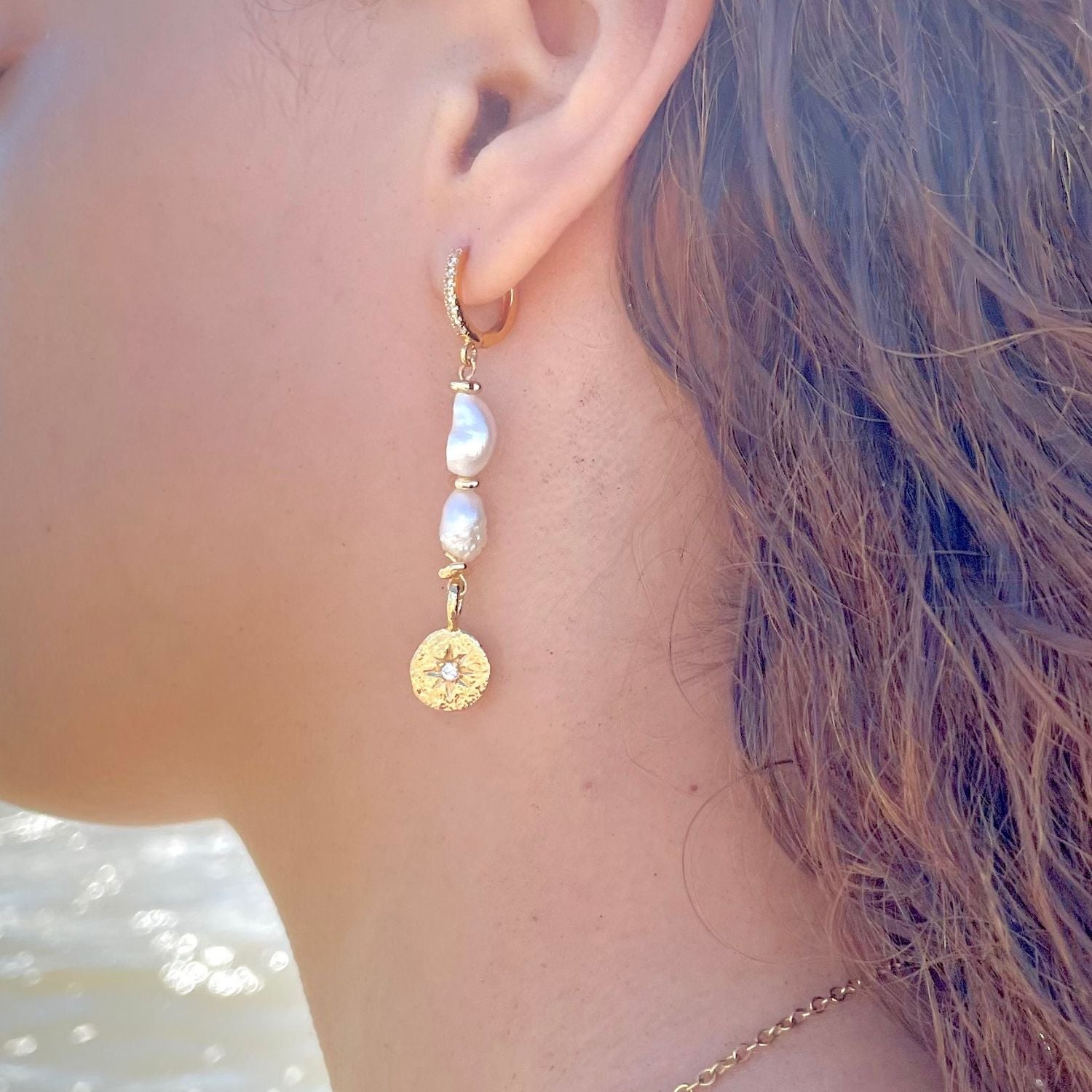 Gold earring with pearls worn by a person with purple hair.