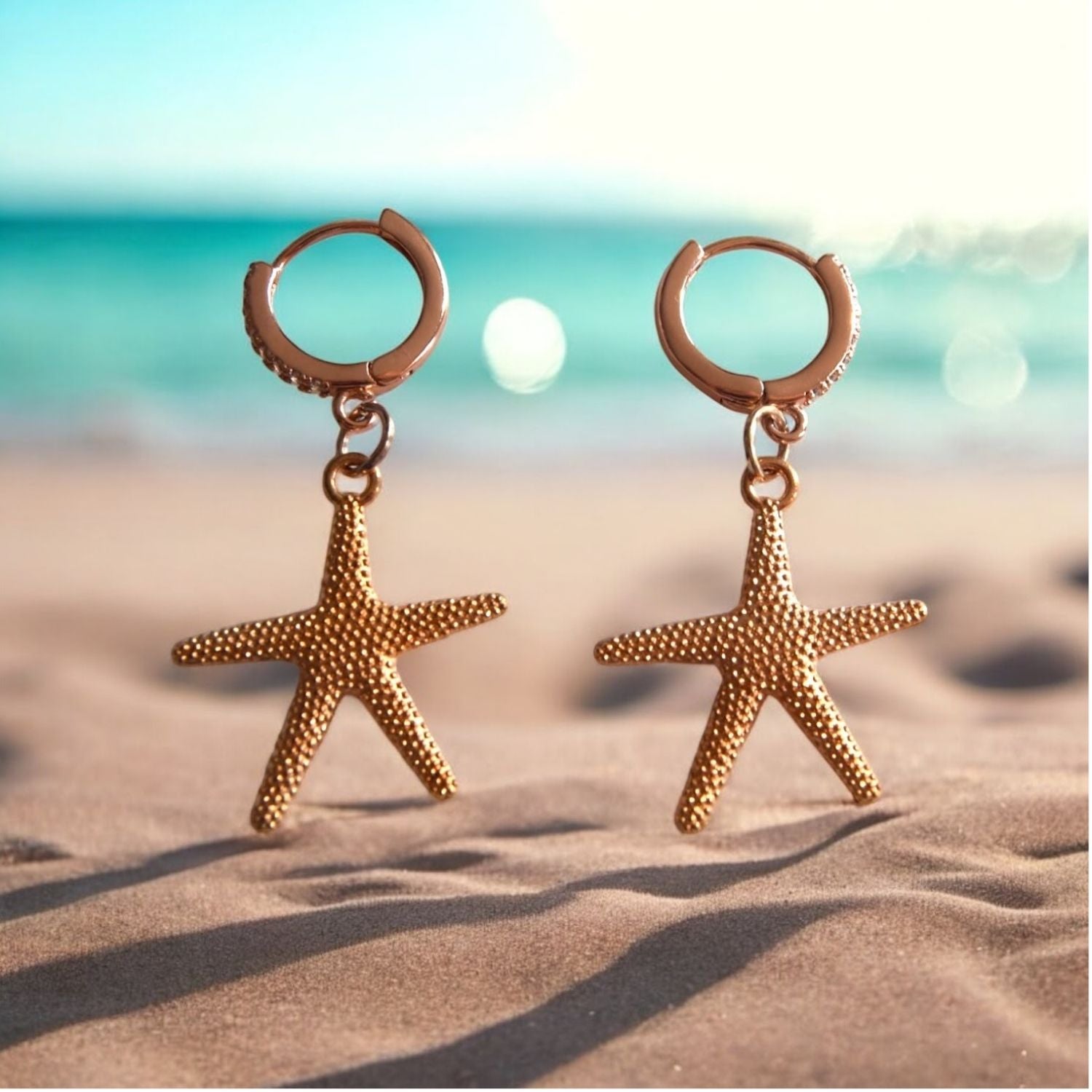 Gold starfish earrings on a sandy beach with ocean in the background