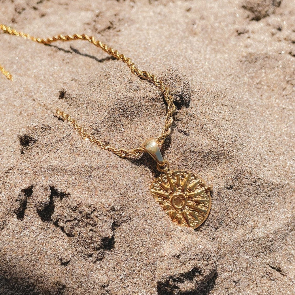 Gold necklace with a heart-shaped pendant on sandy surface