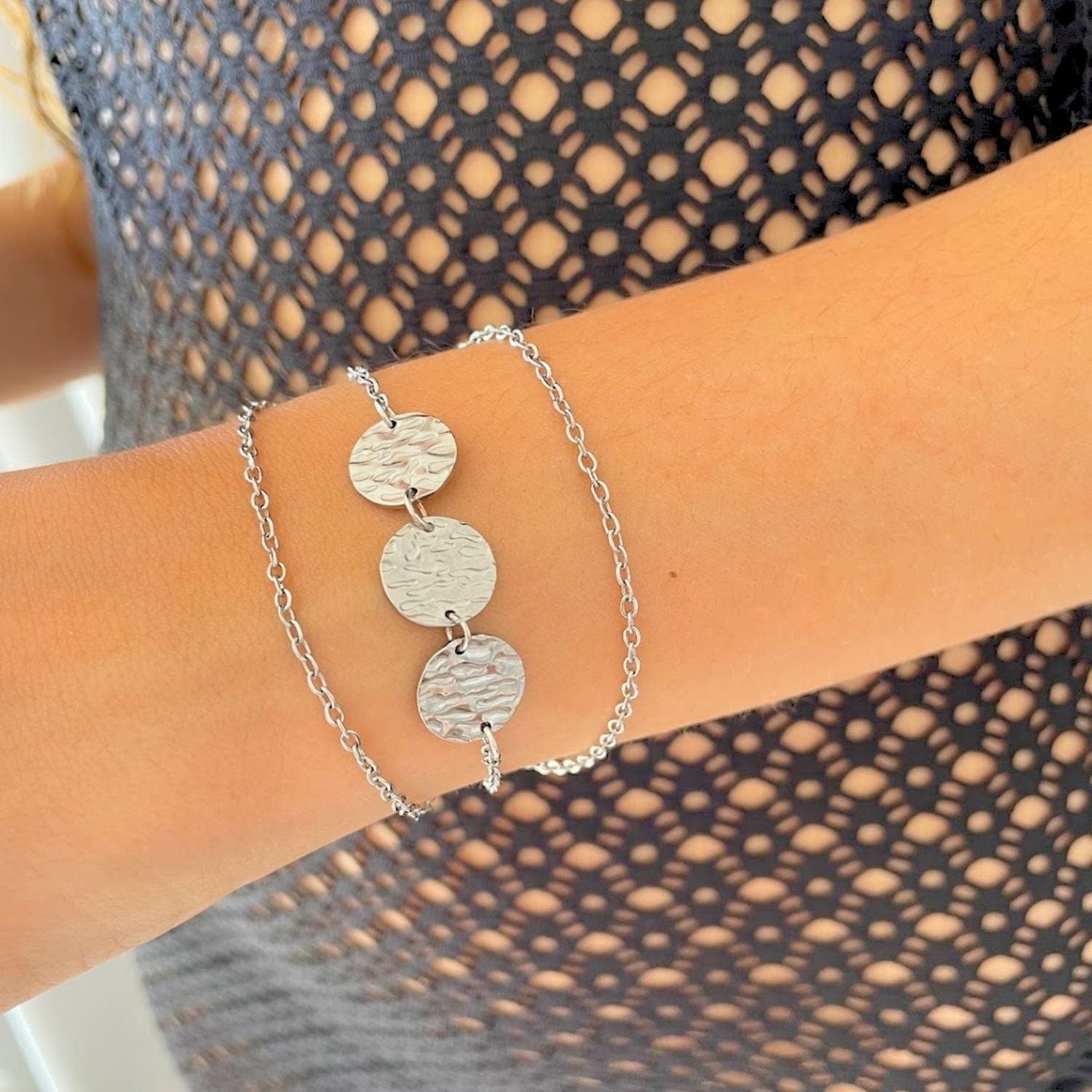 Silver bracelet with circular charms on a wrist against a patterned background