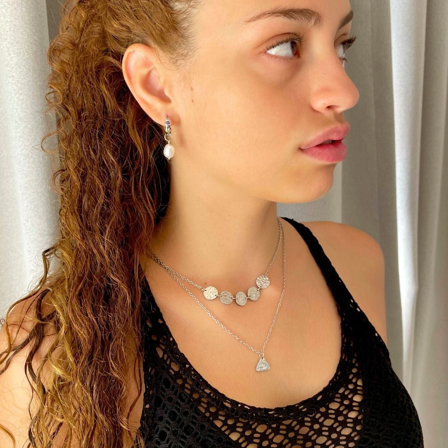Woman wearing layered necklaces and earrings against a neutral background