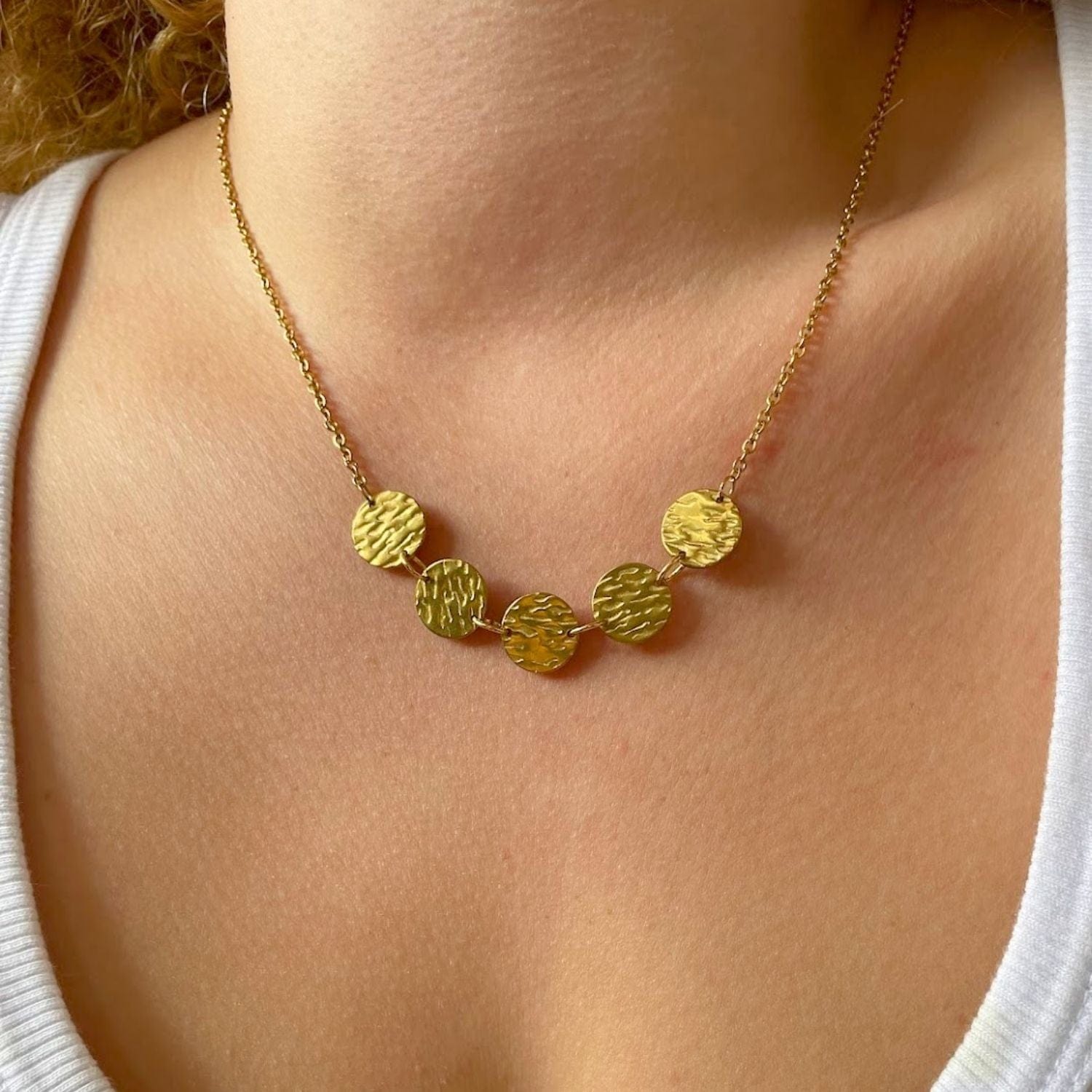 Gold necklace with round pendants on a person wearing a white top.