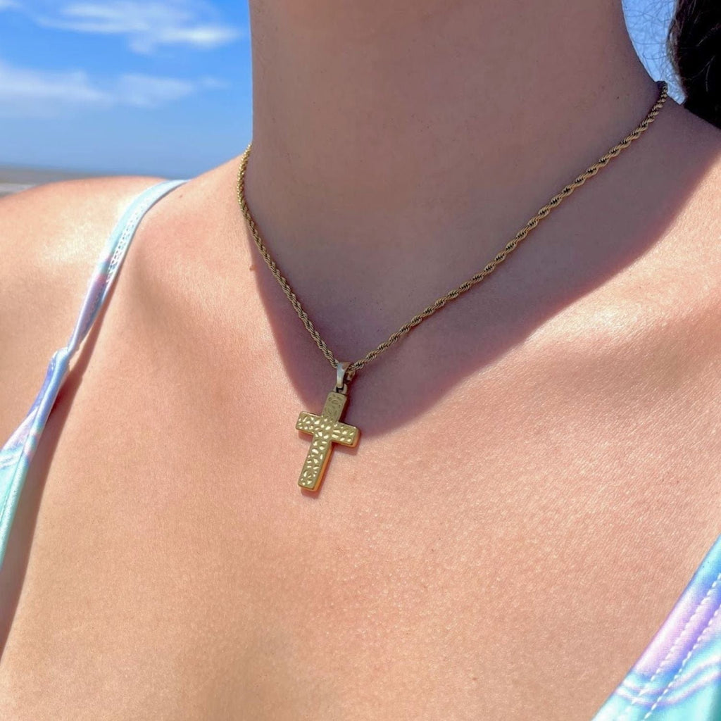 Gold cross necklace on a person with a beach background