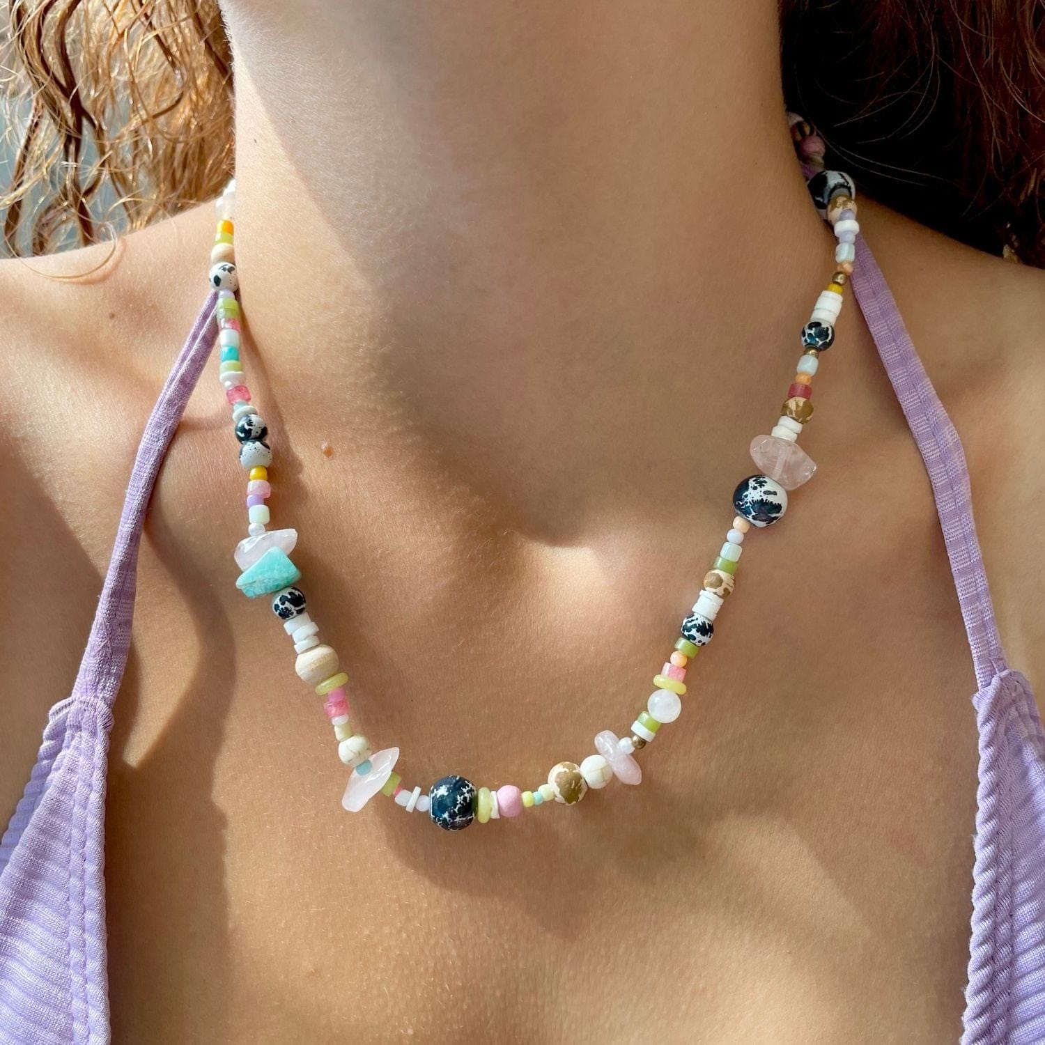 Colorful beaded necklace on a person wearing a light purple top.