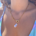Gold necklace with a teardrop pendant on a person wearing a blue bikini.