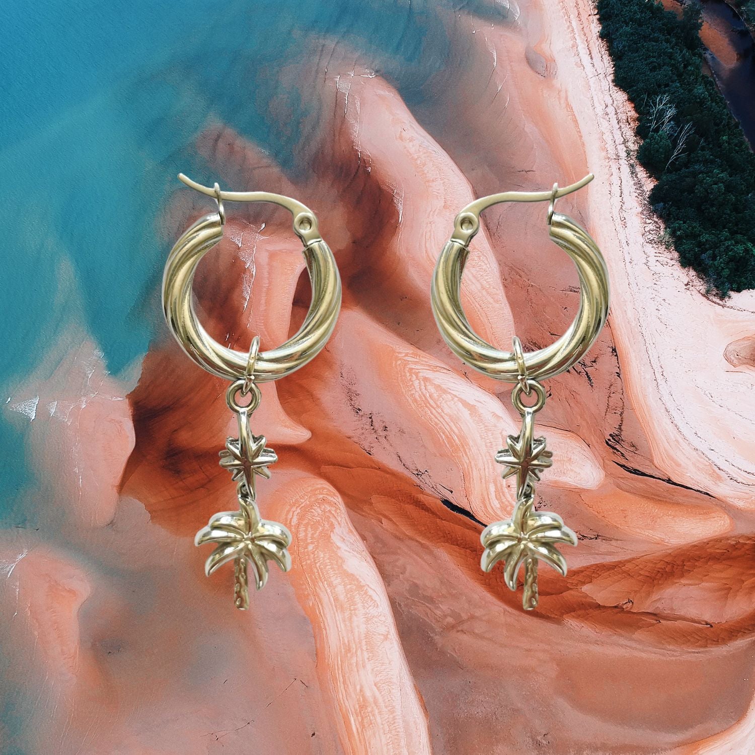Gold hoop earrings with leaf charms on a colorful fabric background
