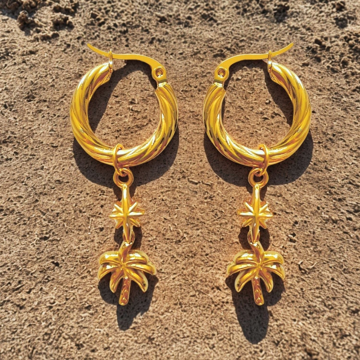 Pair of gold hoop earrings with star-shaped charms on a textured brown surface