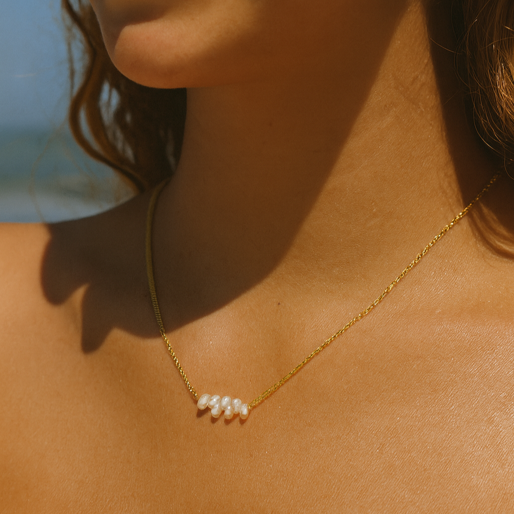 Woman wearing a gold necklace with pearls by the beach