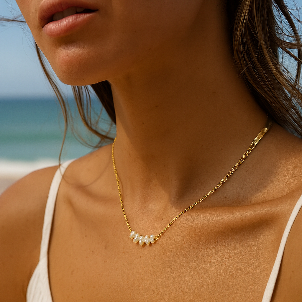 Woman wearing a gold necklace with pearls against a beach background