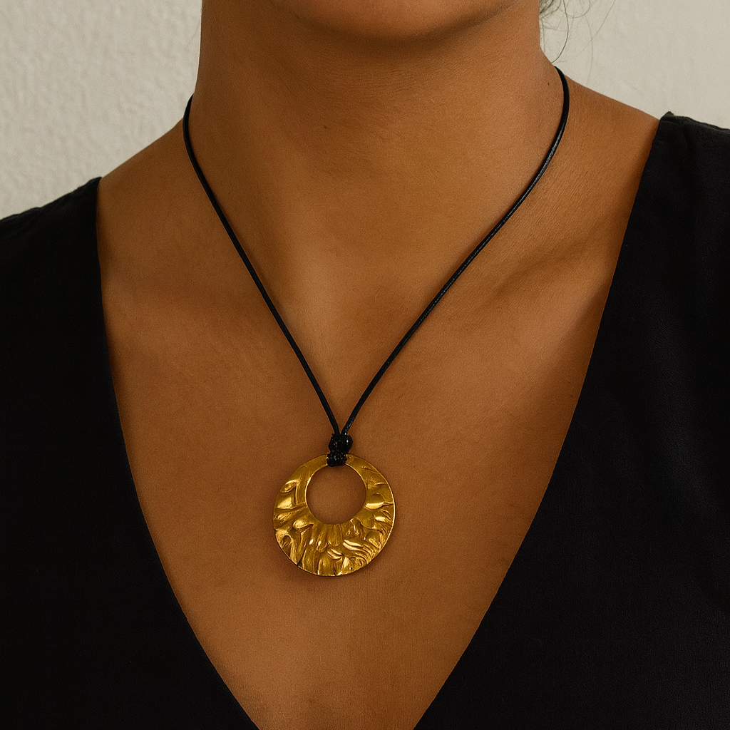 Close-up of a person wearing a gold necklace with a black cord against a neutral background