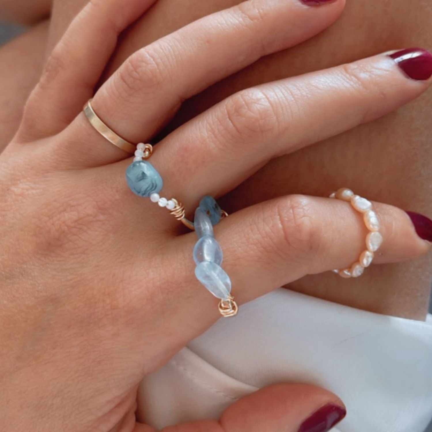 Close-up of a hand wearing multiple rings with gemstones on a neutral background