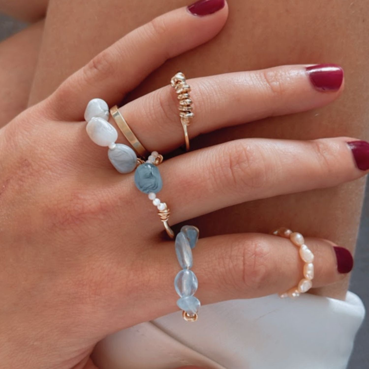 Hand wearing multiple rings with gemstones and pearls on a neutral background