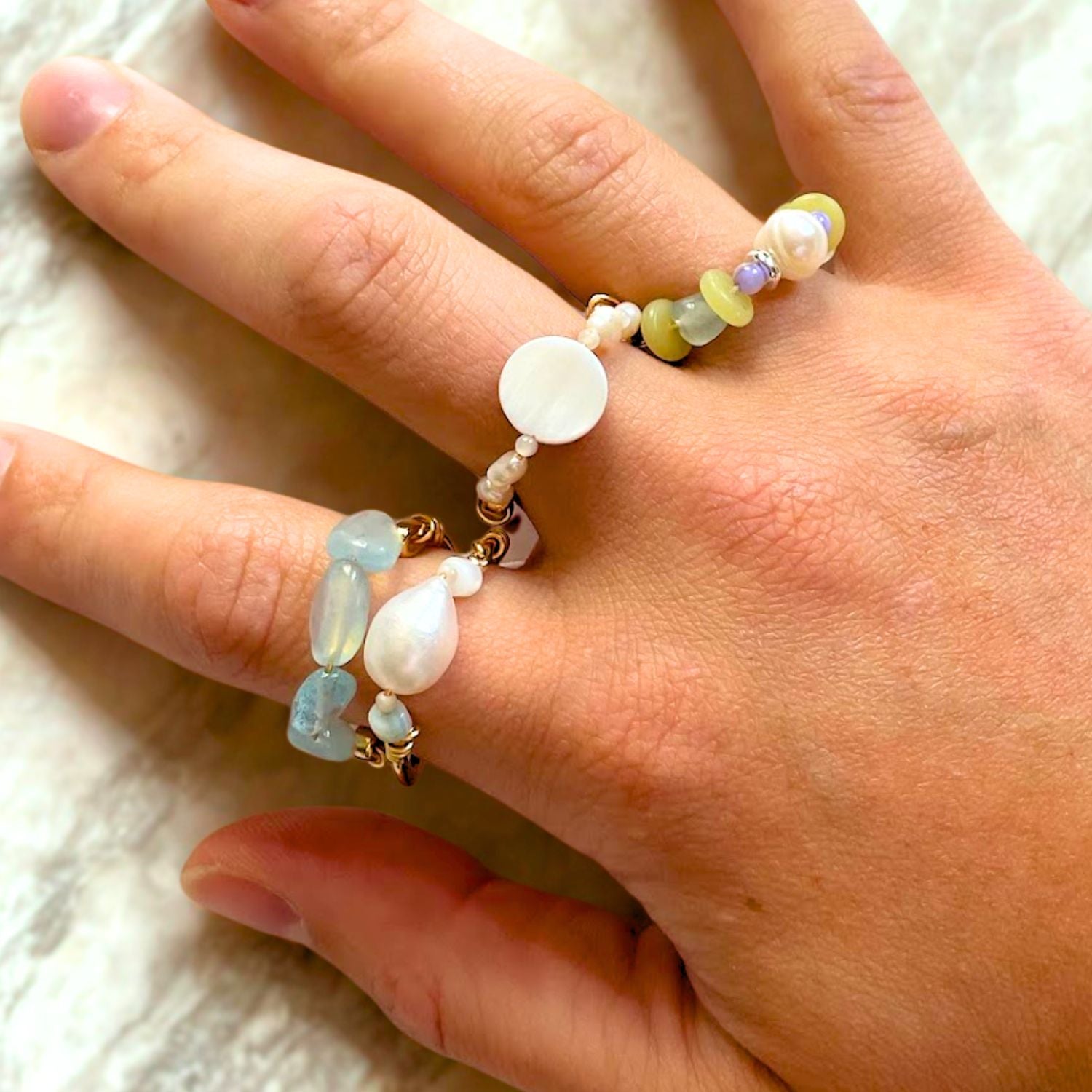 Hand wearing a beaded bracelet with various colored beads on a white fabric background