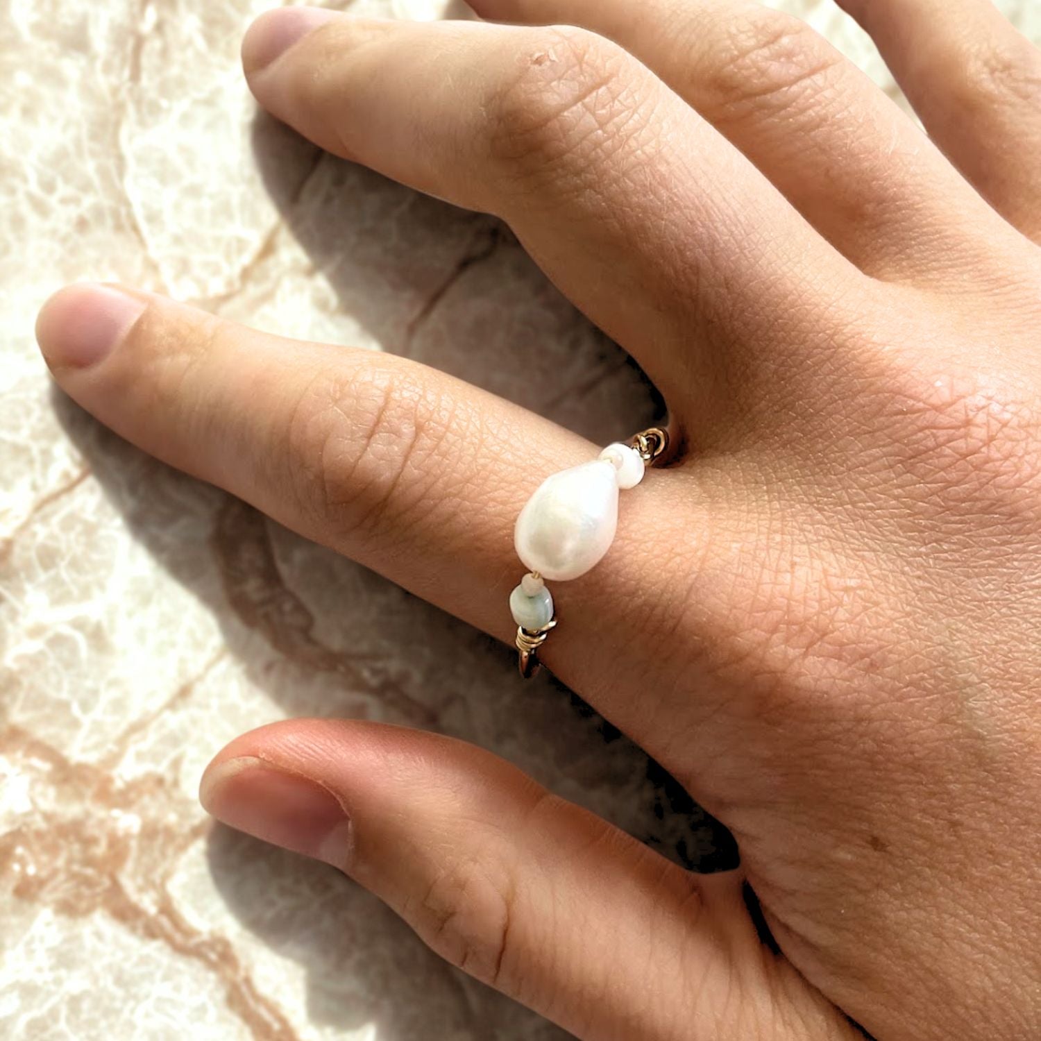Hand wearing a pearl ring on a textured surface