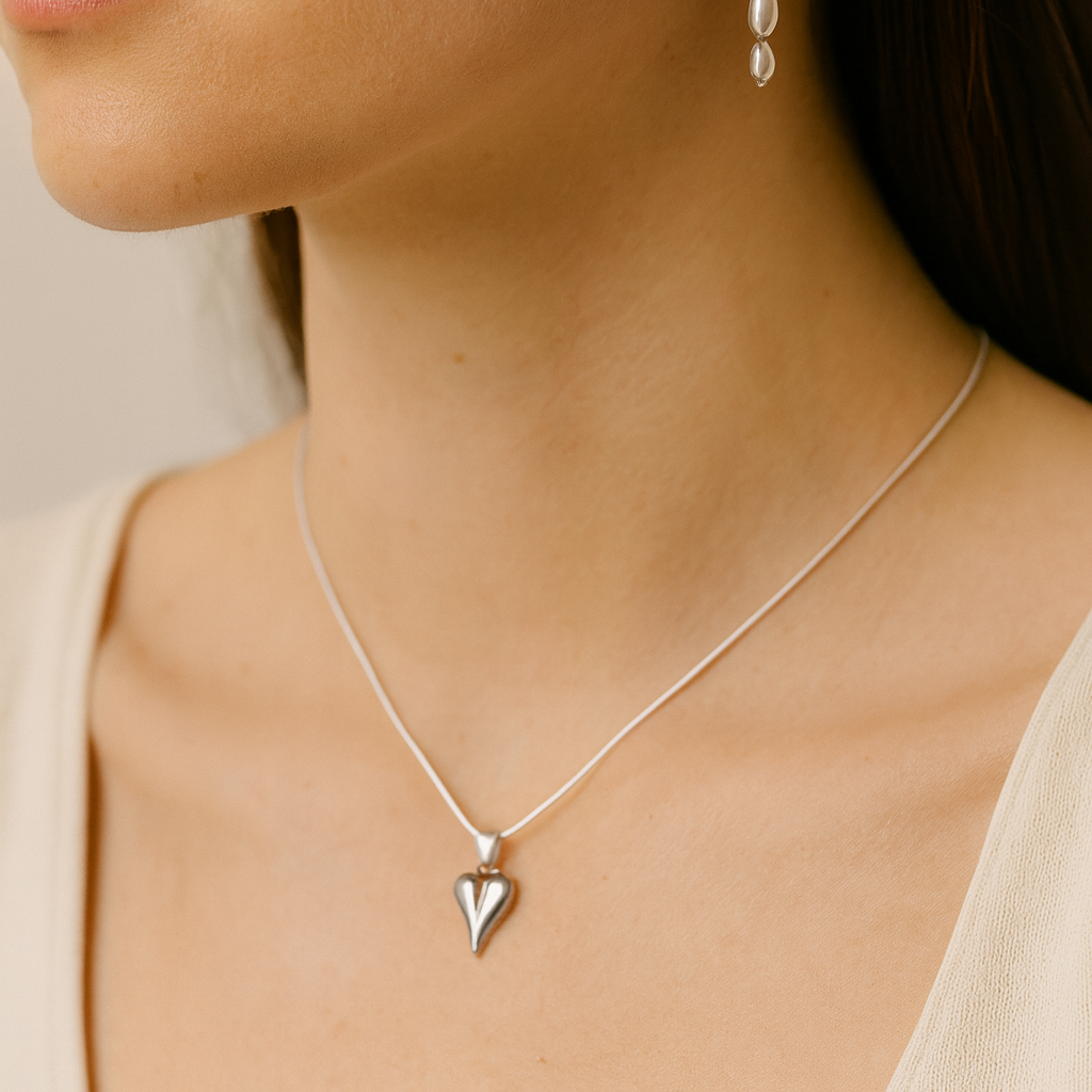 Silver heart pendant necklace on a person wearing a beige top.