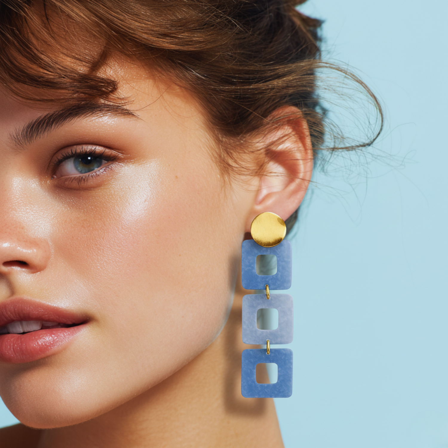 Close-up of a woman wearing blue square earrings with a light blue background