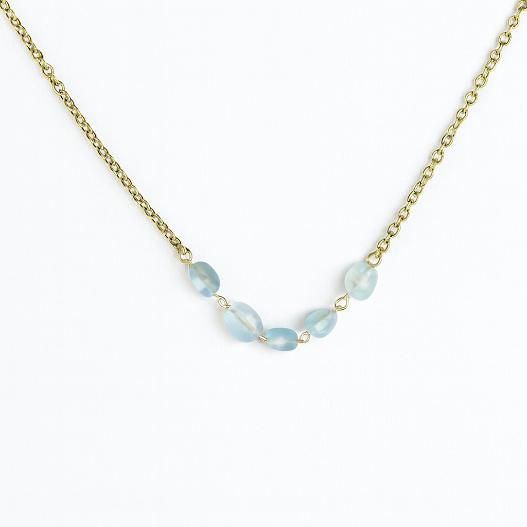 Necklace with light blue beads on a gold chain against a white background
