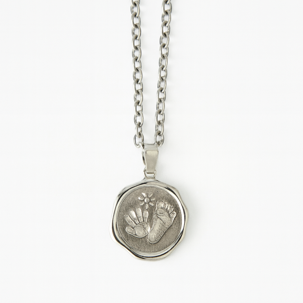 Silver necklace with a pendant featuring hand and footprints on a white background
