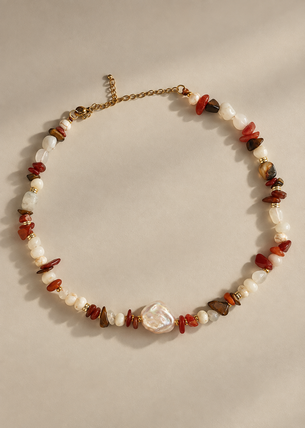 A beaded necklace with white baroque pearls, polished red and brown stone chips, and a central irregular white pearl pendant, displayed on a neutral beige background.