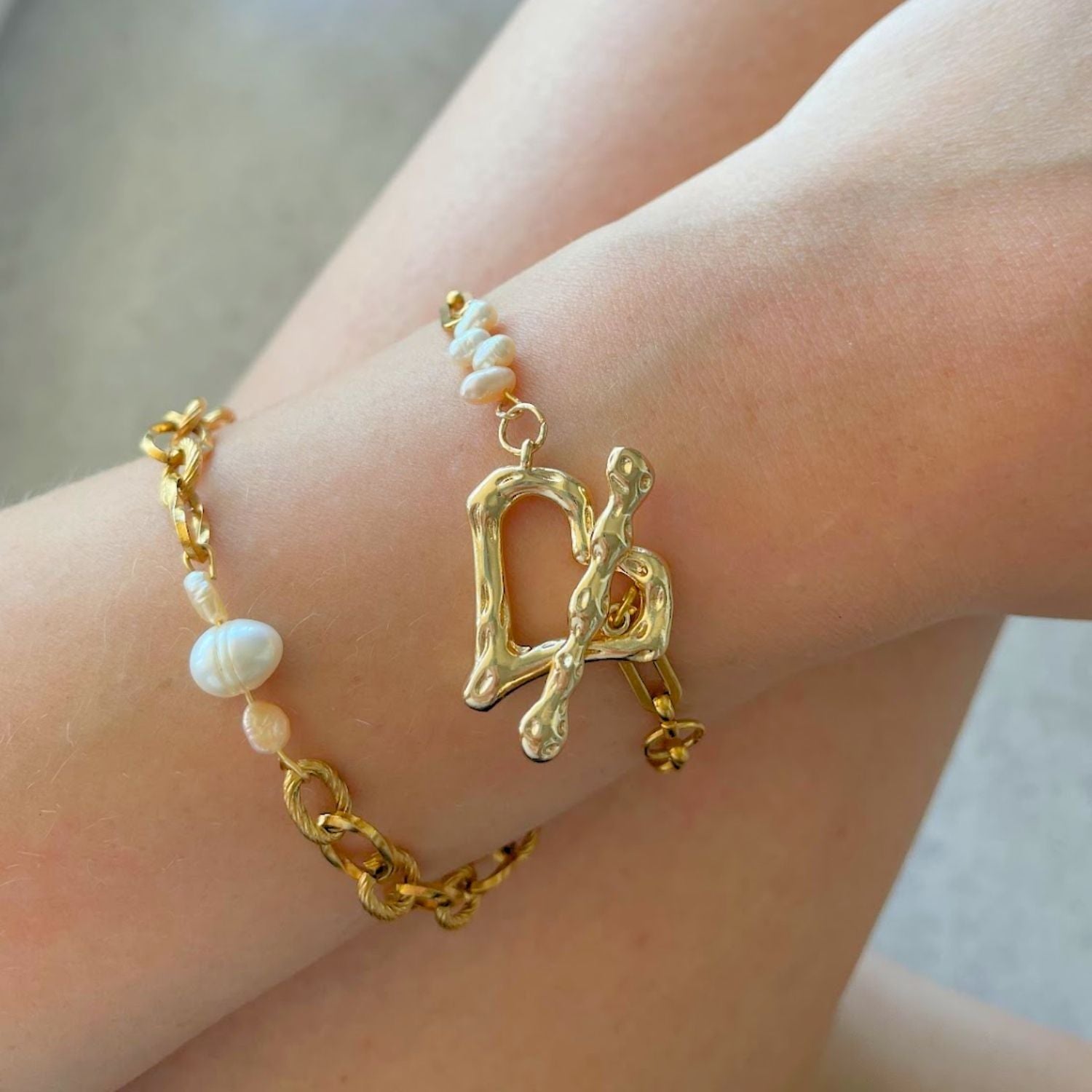 Gold bracelet with pearl beads on a wrist against a neutral background